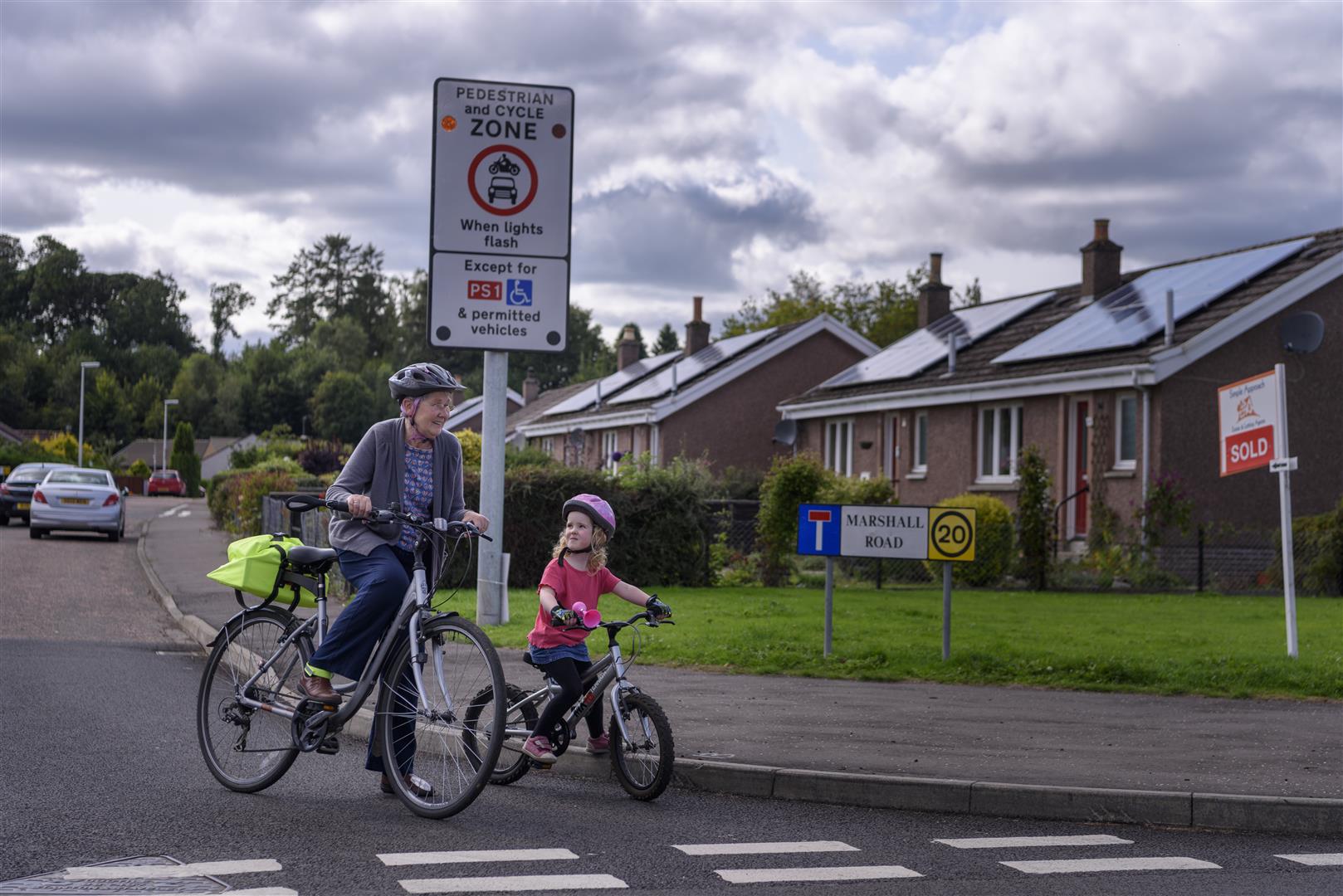 Picture of an elderly person and child on pedal bikes in a residential neighbourhood which is a 20 mph pedestrian and cycle zone. 