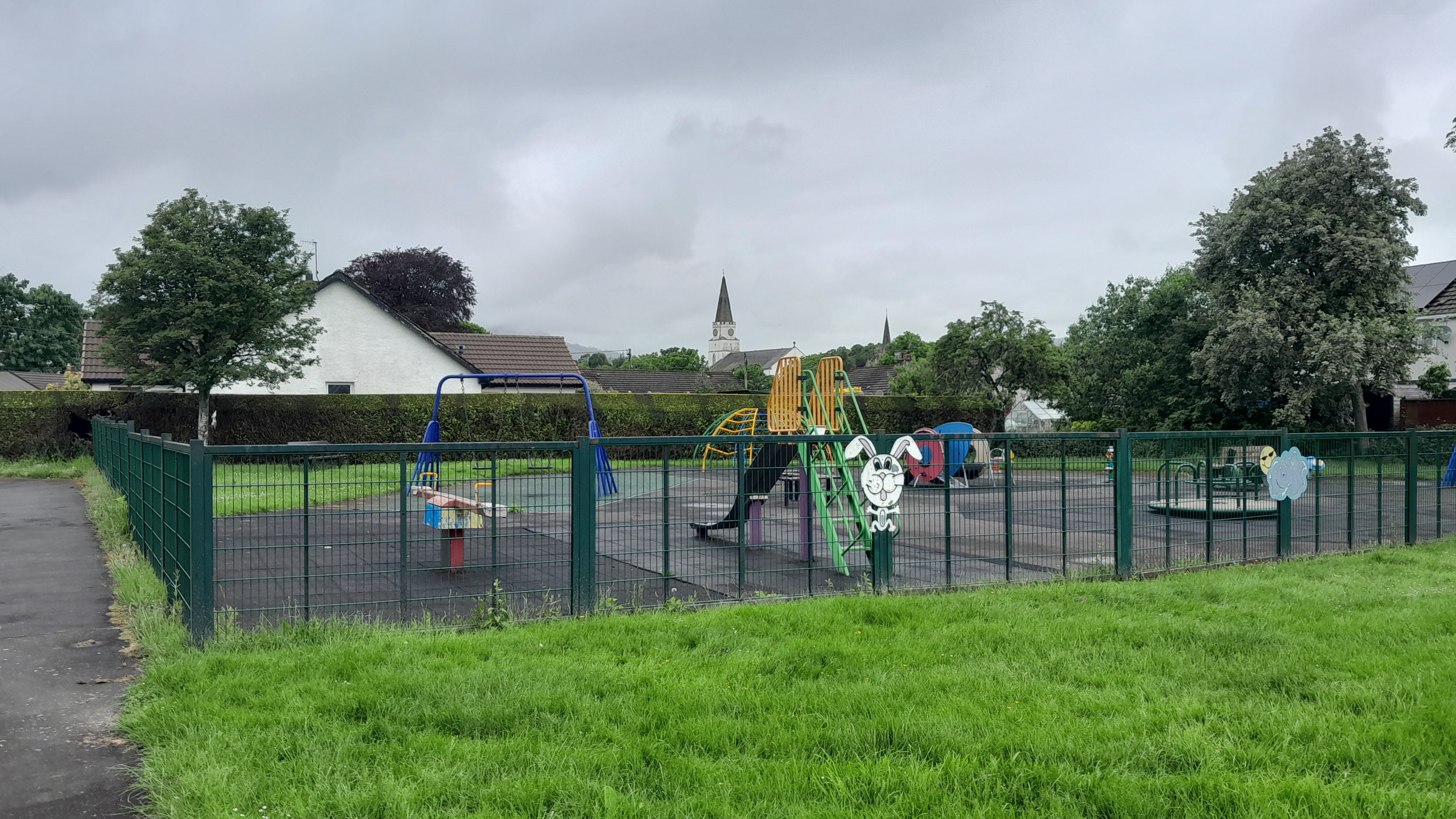 A view of the fenced play area at Legion park with the town clock tower in the background.